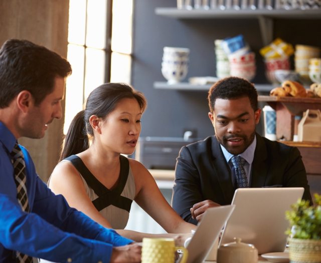 Diverse academic committee sits around laptop at cafe table