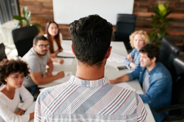 Young white male academic job candidate faces search committee around table